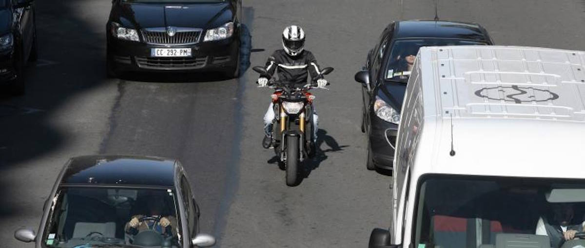 Une moto en interfile entre deux voitures