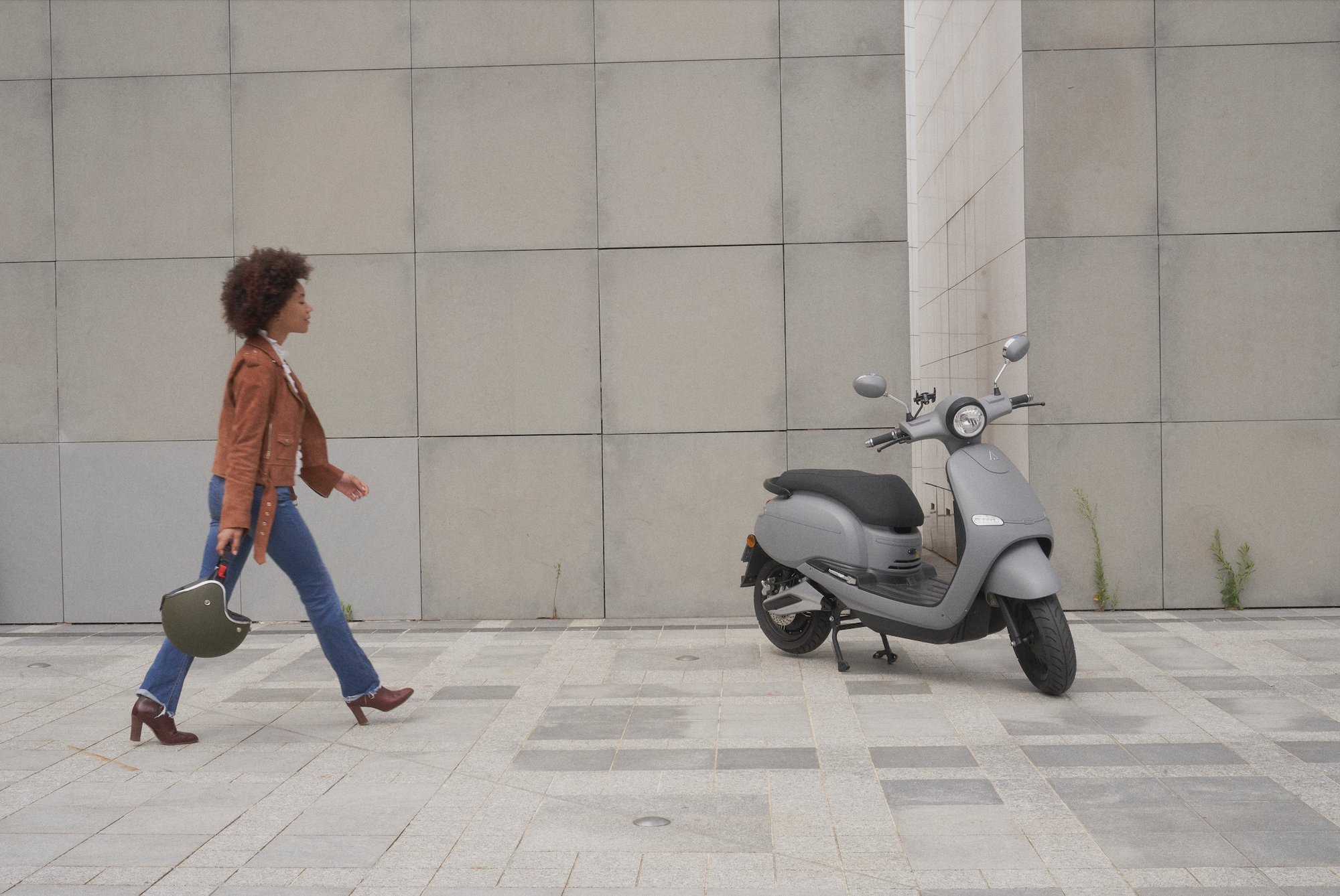 Une femme qui marche avec son casque vers son scooter électrique